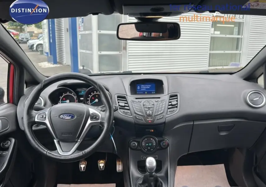 Vue intérieure avant de la Ford Fiesta rouge 2017, tableau de bord avec volant multifonction et boîte manuelle.