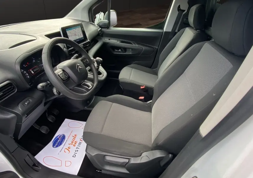 Vue intérieure côté conducteur du Citroën Berlingo blanc, montrant le tableau de bord et les sièges en tissu gris.