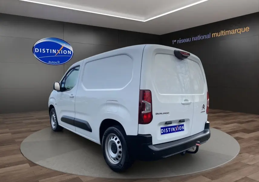 Vue 3/4 arrière droite d'un utilitaire Citroën Berlingo blanc avec hayon fermé et attelage visible en intérieur showroom.