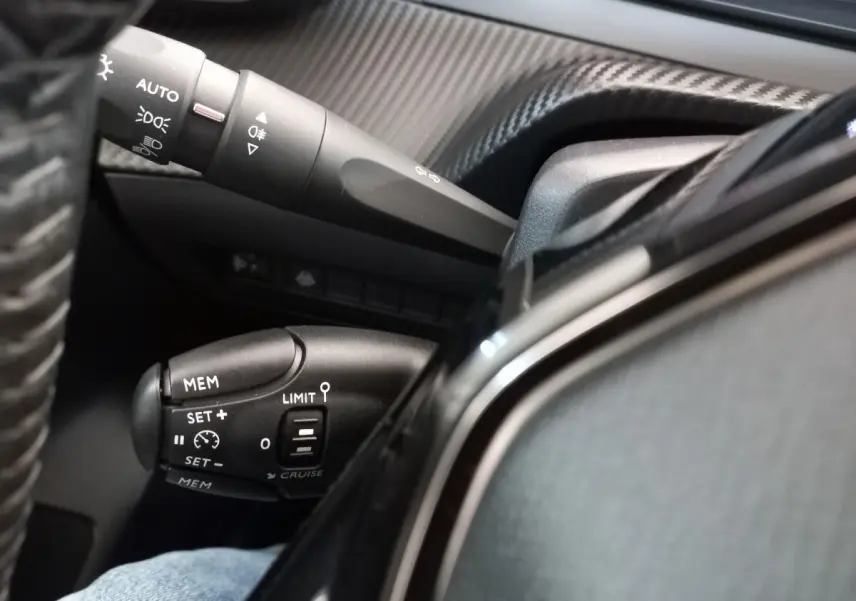 Gros plan sur les commandes de régulateur de vitesse et feux au volant cuir d'une Peugeot 208 PureTech blanche.