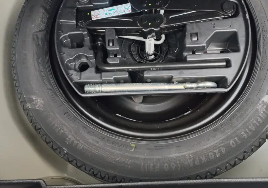 Gros plan sur la roue de secours noire et les outils de bord du coffre d'une Peugeot 208 blanche.