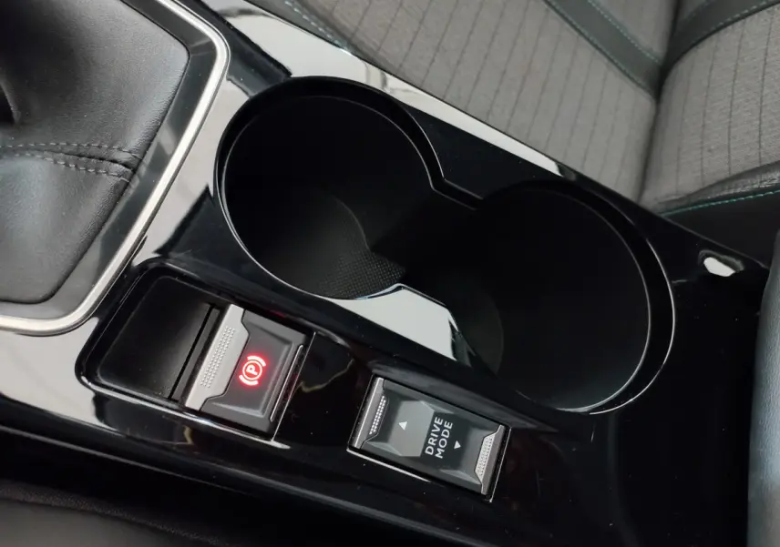Gros plan sur la console centrale noire brillante de la Peugeot 208 blanche, avec frein à main électrique et bouton Drive Mode.