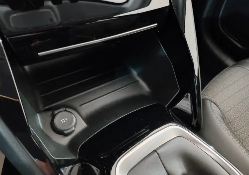 Prise 12V et rangement central noir brillant dans l'habitacle côté droit de la Peugeot 208 blanche PureTech 100 S&S Allure 2021.