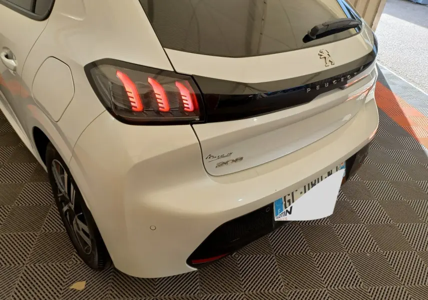 Vue 3/4 arrière droite d'une Peugeot 208 blanche avec feux arrière LED et logo Peugeot sur hayon noir brillant