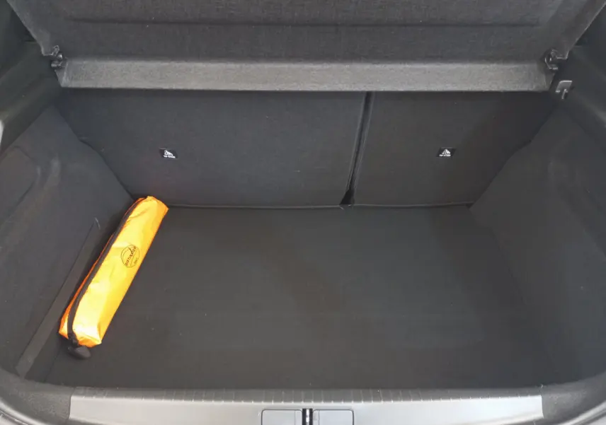 Coffre ouvert de Peugeot 208 blanc, vue intérieure montrant un rangement spacieux avec une trousse de sécurité orange sur la gauche.