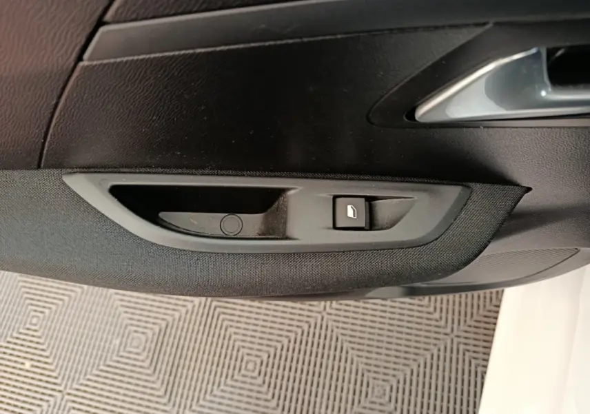 Détail de la commande de lève-vitre électrique sur la porte côté conducteur d'une Peugeot 208 électrique blanche.