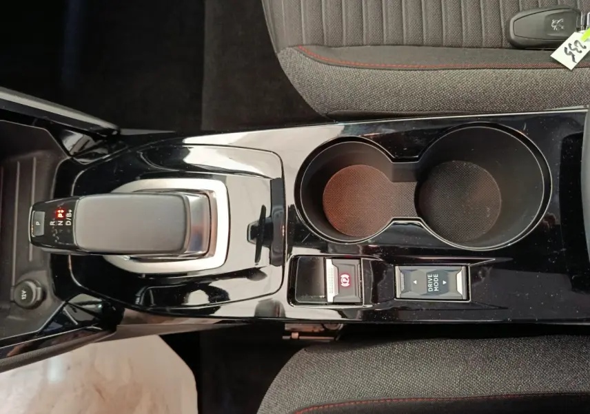 Vue plongeante sur la console centrale noire brillante de la Peugeot 208 électrique avec levier de vitesses et porte-gobelets.