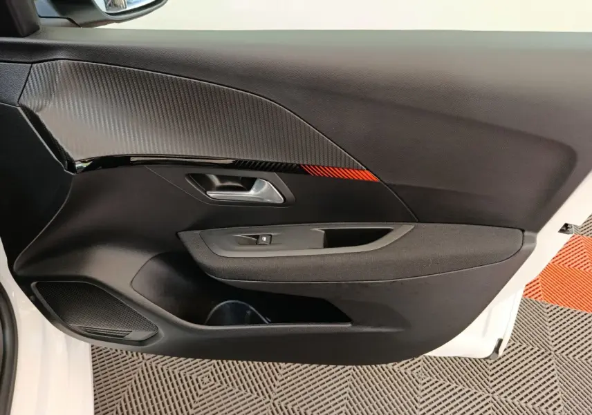 Gros plan sur la porte intérieure côté conducteur de la Peugeot 208 électrique blanche, avec insert noir et détail rouge.