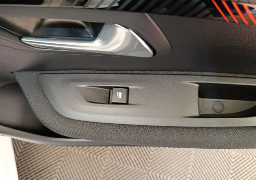 Détail de la commande de lève-vitre et poignée intérieure sur la porte côté conducteur d'une Peugeot 208 blanche électrique.
