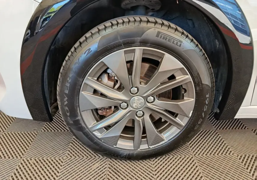 Gros plan sur la roue avant droite d'une Peugeot 208 électrique blanche, avec jante alliage et pneu Pirelli.