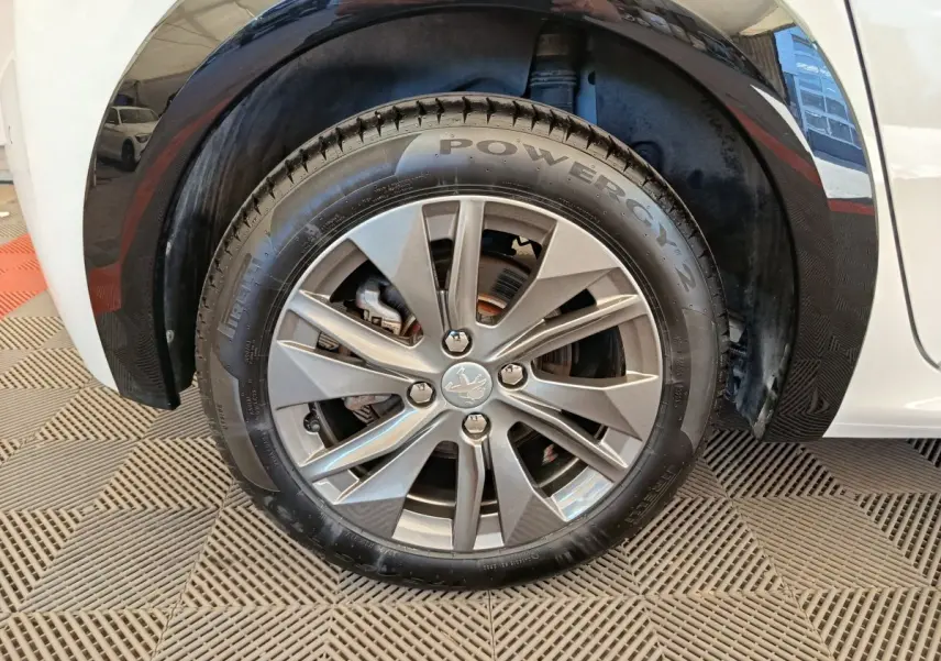 Gros plan sur la roue avant droite d'une Peugeot 208 électrique blanche, avec jante alliage et logo lion central.