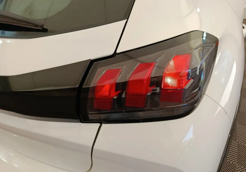Gros plan sur le feu arrière droit rouge d'une Peugeot 208 électrique blanche, soulignant le design moderne.