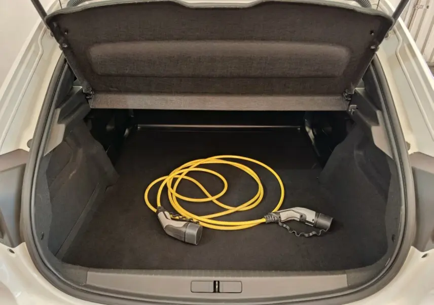 Coffre ouvert d’une Peugeot 208 électrique blanche, vue arrière, avec câble de recharge jaune visible à l’intérieur.