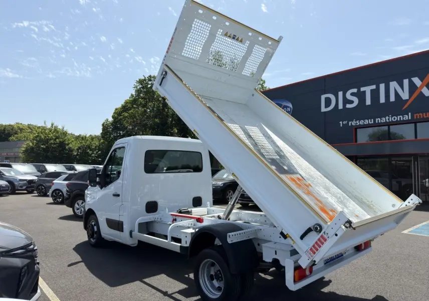 Renault Master blanc vue 3/4 arrière avec benne relevée sur parking ensoleillé.