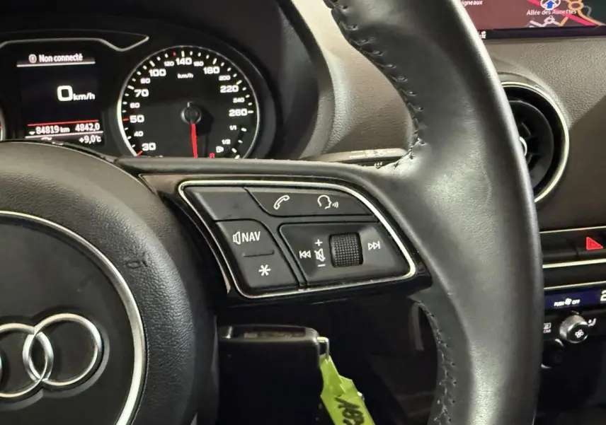 Gros plan sur le volant cuir noir de l'Audi A3 2018 avec commandes audio et tableau de bord affichant la navigation.