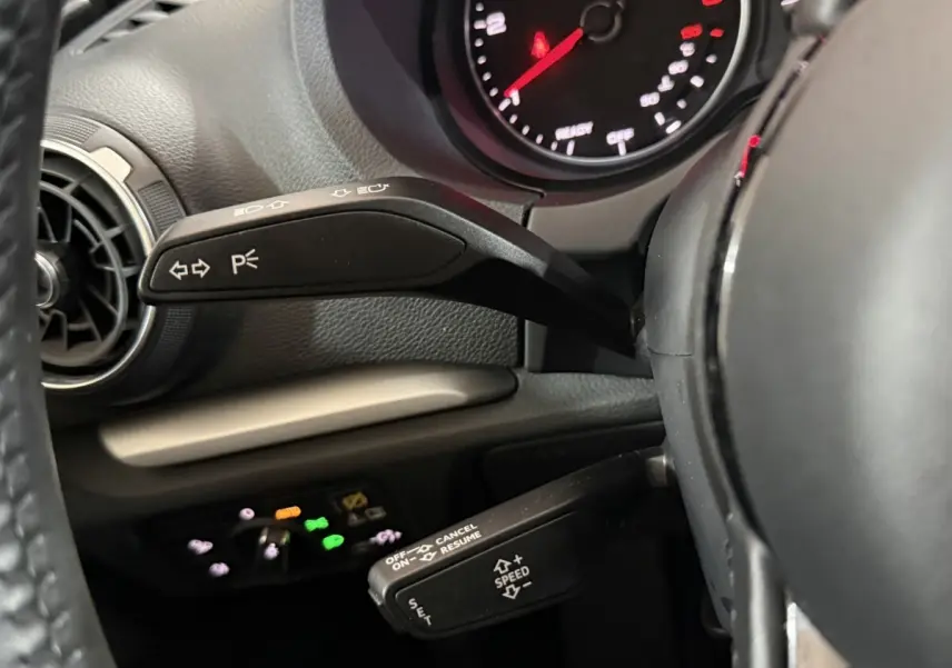 Gros plan sur les commandes au volant d'une Audi A3 bleu 2018, mettant en valeur les leviers de clignotants et régulateur de vitesse.