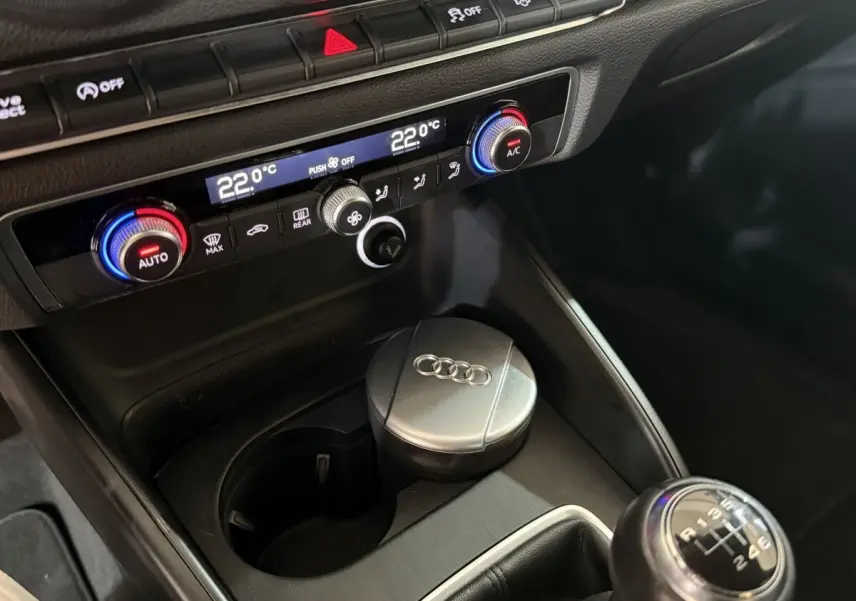 Gros plan sur la console centrale de l'Audi A3 bleu 2018, montrant la climatisation digitale et le levier de vitesses manuel.