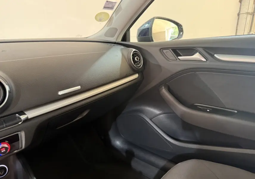 Intérieur côté passager de l'Audi A3 bleu 2018, tableau de bord noir avec aérateurs ronds et garnitures argentées.