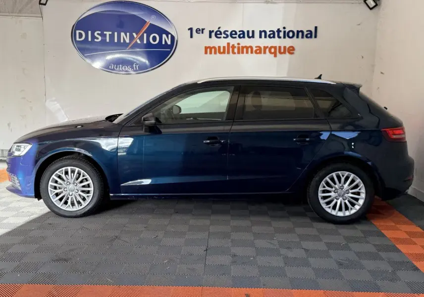 Profil côté gauche d'une Audi A3 bleu foncé 2018 garée en intérieur sur sol à damiers gris et orange.
