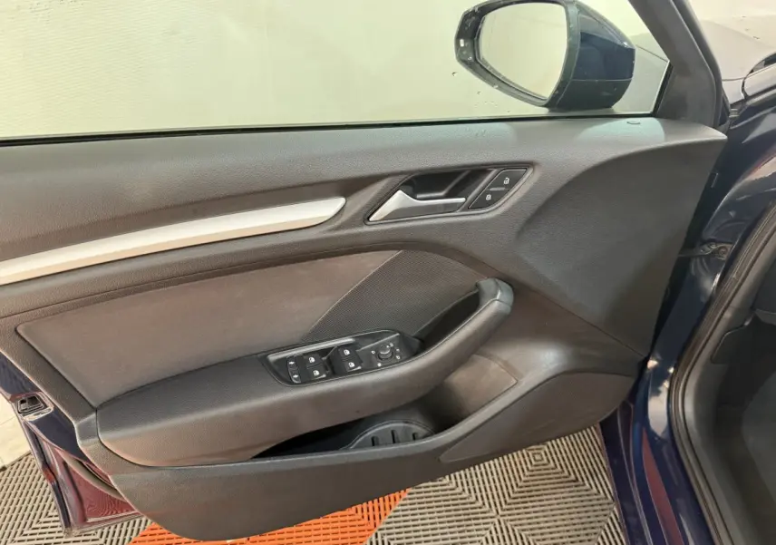 Vue rapprochée de la porte avant gauche d'une Audi A3 bleu 2018, avec commandes électriques et miroir extérieur visible.