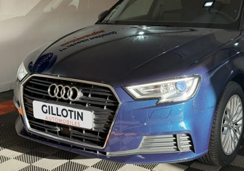 Vue 3/4 avant droit d'une Audi A3 bleu métallisé avec calandre hexagonale et phares LED allumés.