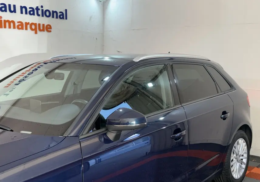 Vue de profil côté gauche d'une Audi A3 bleu foncé 2018 avec rétroviseur et jantes visibles dans un showroom.