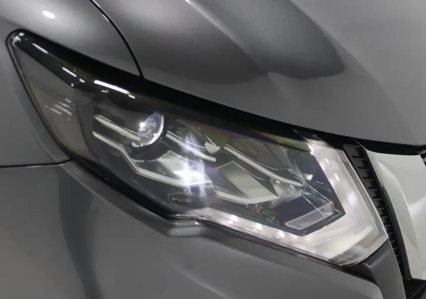 Gros plan sur le phare avant droit du Nissan X-TRAIL gris métallisé, soulignant ses lignes modernes et LED.