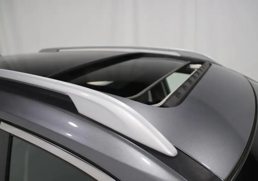 Détail du toit ouvrant ouvert et des barres de toit sur un Nissan X-TRAIL gris métallisé.