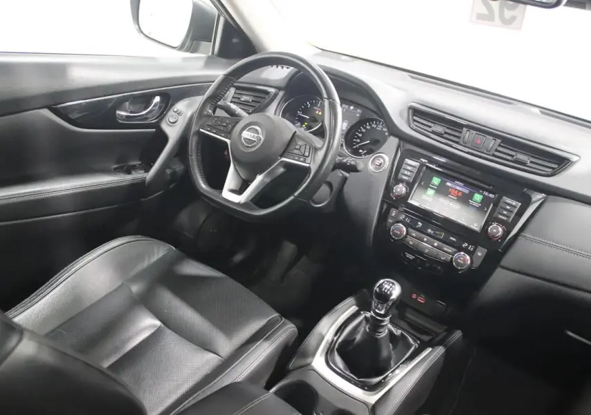 Vue intérieure côté conducteur du Nissan X-TRAIL 1.7 D 150 avec volant cuir, sièges noirs et boîte manuelle.