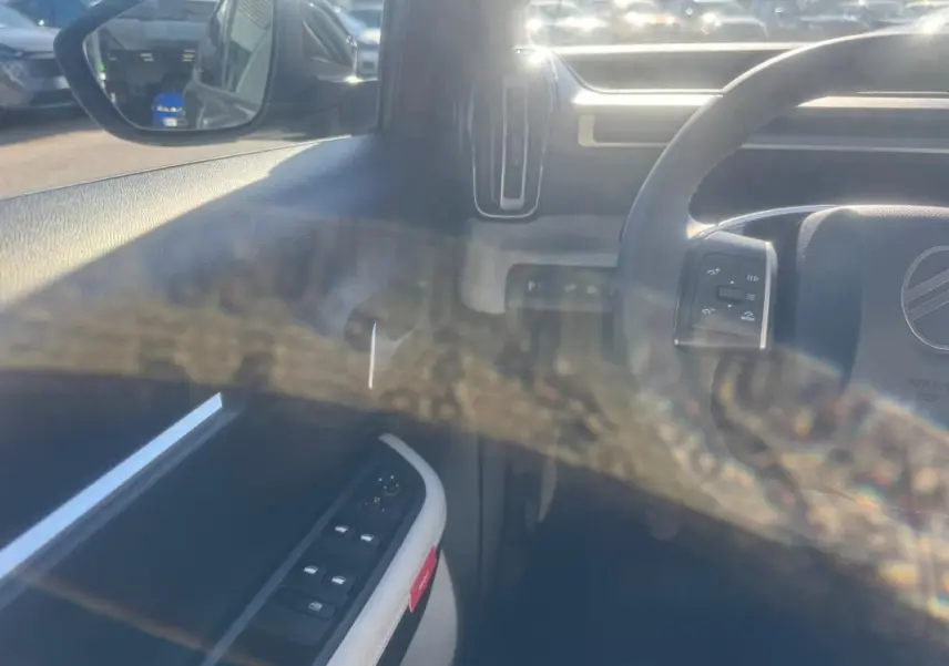 Vue intérieure côté conducteur de la Citroën C3 gris 2025, avec commandes des vitres et rétroviseur électrique visibles.