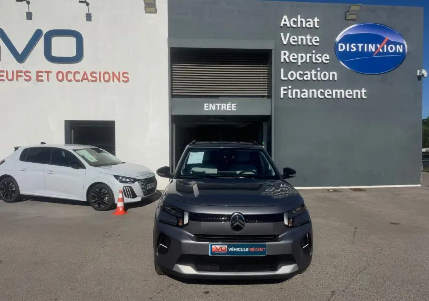 Citroën C3 gris vue de face, avec barres de toit et jantes alliage 17 pouces, devant un bâtiment de vente auto.