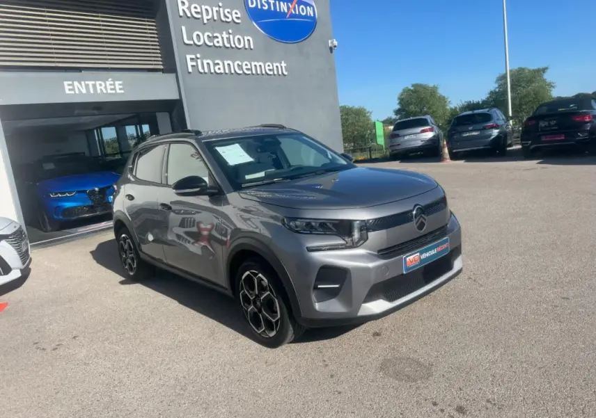 Citroën C3 gris 3/4 avant droit avec barres de toit et jantes alliage 17 pouces, stationnée devant un concessionnaire.