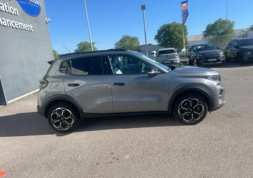 Vue de profil côté gauche d'une Citroën C3 gris métallisé 2025 avec jantes alliage 17 pouces et barres de toit noires.