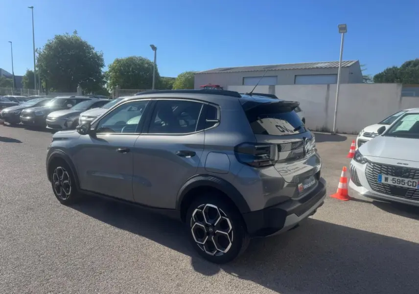 Vue 3/4 arrière droite d'une Citroën C3 gris 2025 avec jantes alliage 17 pouces et barres de toit noires.
