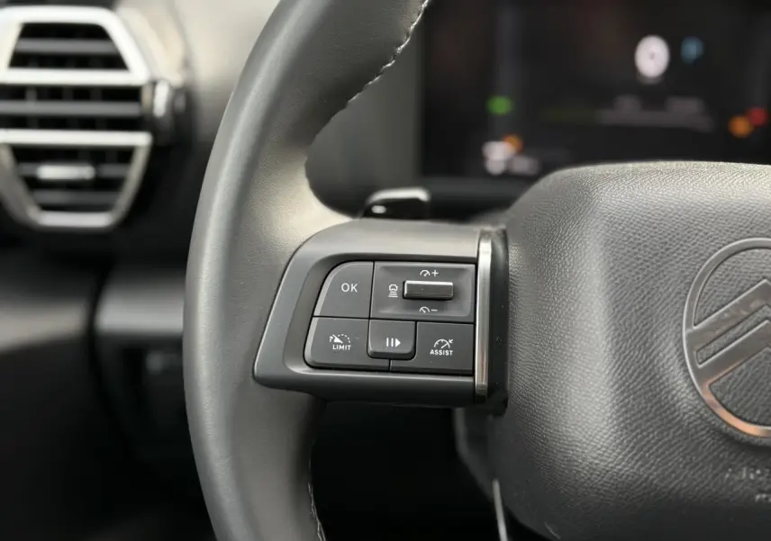 Gros plan sur les commandes au volant côté gauche en cuir noir du Citroën C4 Hybrid gris Mercury, avec aérateur en arrière-plan.