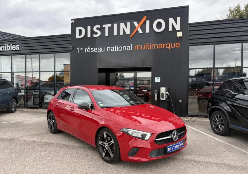 Vue 3/4 avant d'une Mercedes Classe A rouge avec jantes alliage noires, garée devant un bâtiment Distinxion.
