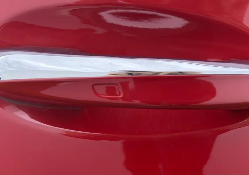 Gros plan sur la poignée de porte chromée d'une Mercedes Classe A rouge, finition Progressive Line.