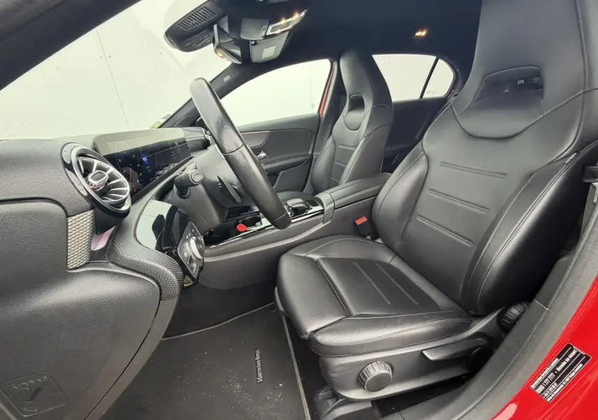 Vue intérieure côté conducteur de la Mercedes Classe A rouge, sièges cuir noir et tableau de bord moderne avec écran tactile.