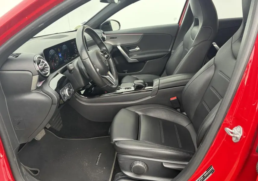 Vue intérieure côté conducteur d'une Mercedes Classe A rouge, mettant en valeur les sièges cuir noirs et le tableau de bord moderne.