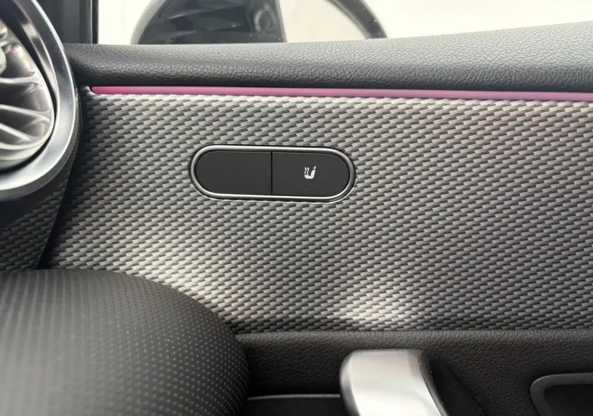 Gros plan sur la commande de siège chauffant intégrée dans la garniture effet carbone à l'intérieur d'une Mercedes Classe A rouge.