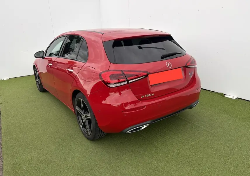 Vue 3/4 arrière gauche d'une Mercedes Classe A 180d rouge avec vitres teintées et jantes alliage noires à 5 branches.