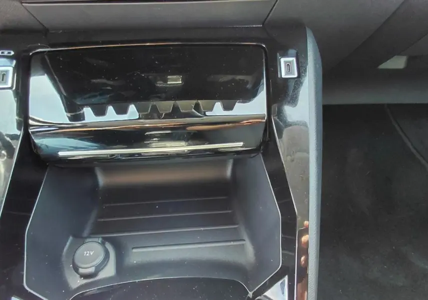 Gros plan sur la console centrale noire brillante de la Peugeot 208 Hybrid 110 ch, avec prise 12V visible.
