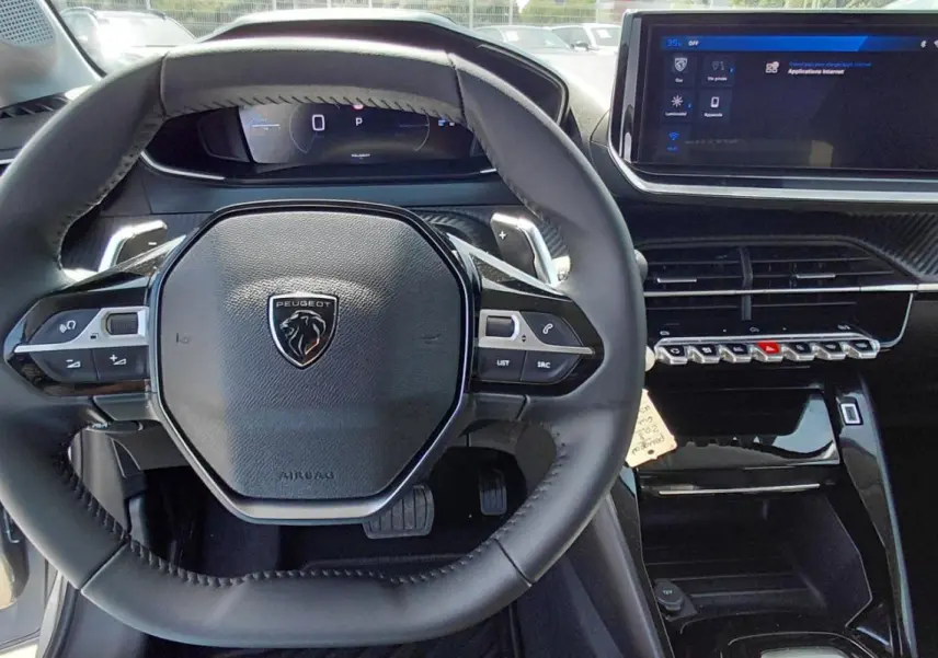 Vue intérieure centrée sur le volant cuir noir et le cockpit numérique de la Peugeot 208 gris 2025 Hybrid Allure.