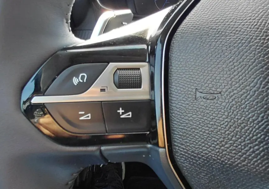 Gros plan sur les commandes gauche du volant en cuir noir du Peugeot 208 gris, avec boutons de volume et fonction mains libres.
