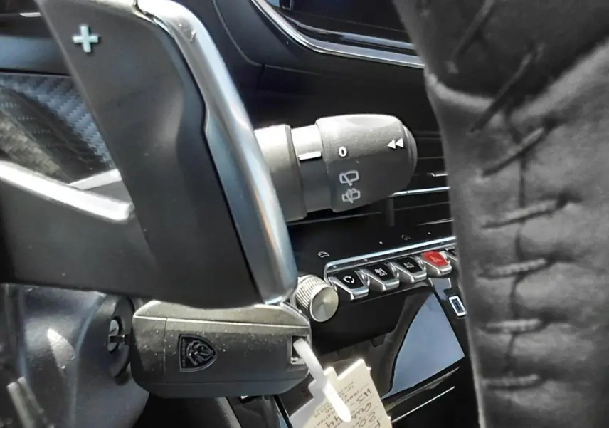 Gros plan sur le volant et la commande de clignotant d’une Peugeot 208 Hybrid gris, avec détails des boutons du tableau de bord.