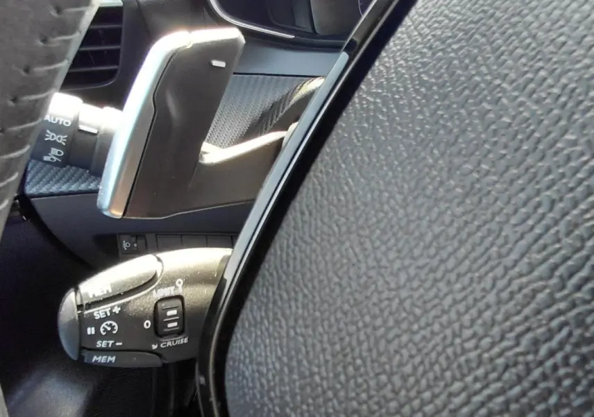Gros plan sur le volant et la commande de régulateur de vitesse d’une Peugeot 208 gris, intérieur moderne et texturé.