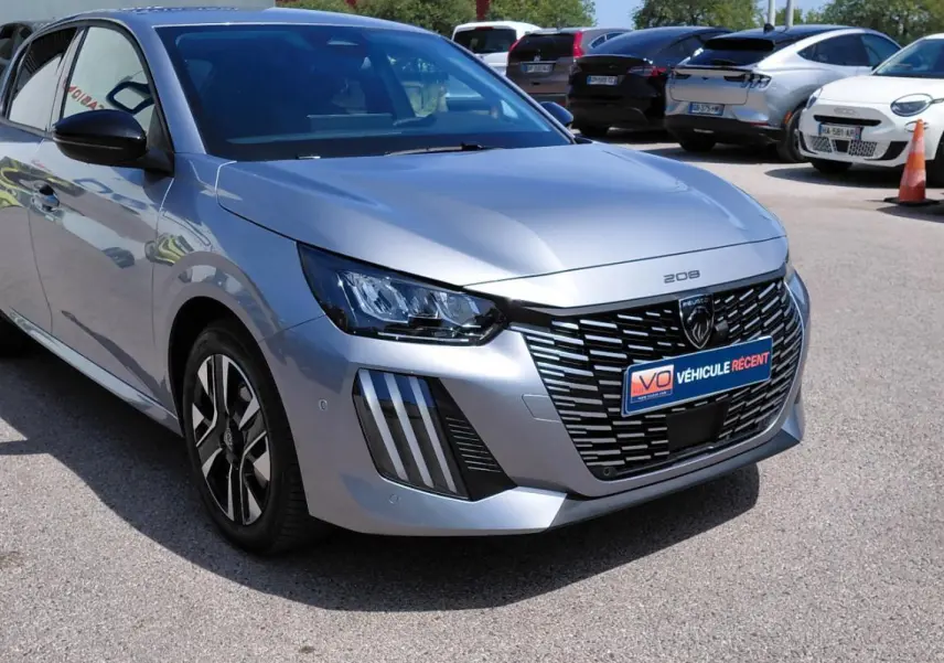 Peugeot 208 gris vue 3/4 avant droit, avec calandre noire distinctive et jantes alliage 16 pouces.