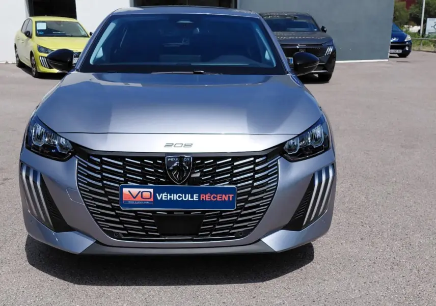 Vue avant d'une Peugeot 208 gris métallisé 2025 avec calandre noire distinctive et feux LED en forme de griffes.