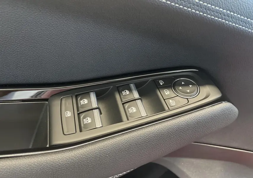 Gros plan sur les commandes de lève-vitres et rétroviseurs sur la porte côté conducteur en finition textile gris foncé.