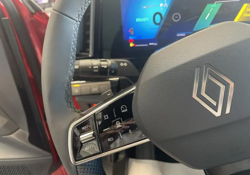 Gros plan sur le volant gris textile du Renault Rafale 2025, avec commandes intégrées et tableau de bord digital en arrière-plan.